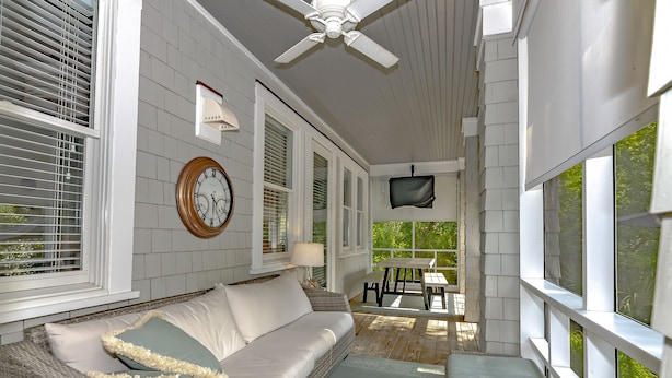 A covered porch with a white wicker sofa, a table, and a ceiling fan. - Luxury Getaway on Bald Head Island - 5-Star Property - Discounts for September (Bald Head Island)