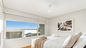 Een slaapkamer met een groot raam, een bed met wit beddengoed en een ingelijste foto aan de muur.
