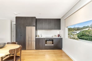 A modern kitchen with dark wood cabinets, a stainless steel refrigerator, and an oven. - Newly built luxurious 2BR apartment situated only minutes to the beach.  (Hyams Beach)