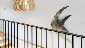 Een trap met een houten leuning en zwarte spijbels, een wandlamp en een groot, gebogen metalen sculptuur.