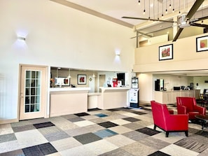 A hotel lobby with a reception desk, a water cooler, a seating area with red chairs, and a check-in counter.