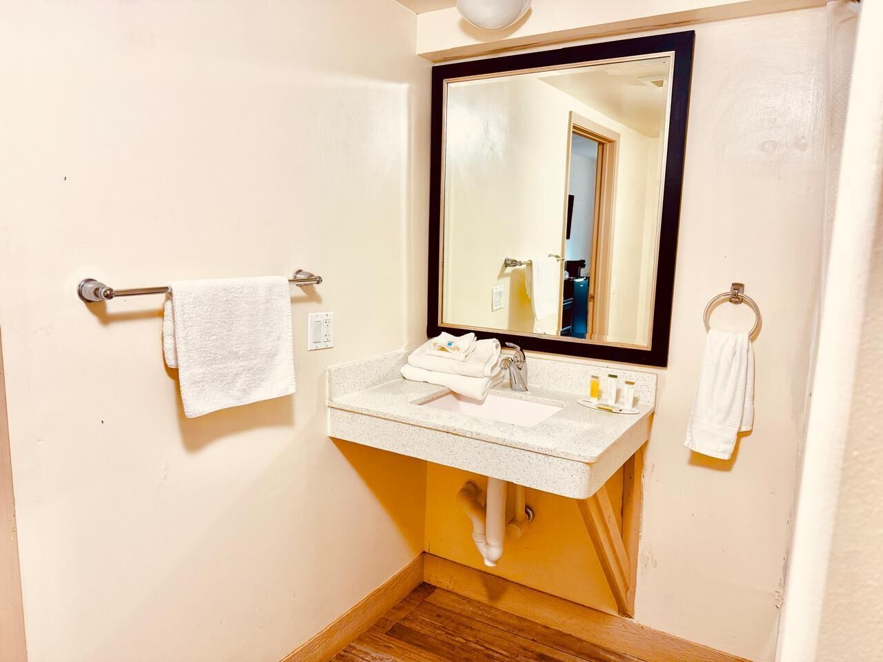 Ein Badezimmer mit Waschbecken, Spiegel, Handtuchhalter und Holzboden.