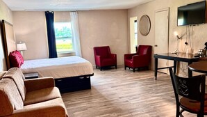 Een hotelkamer met een bed, twee rode stoelen, een tafel, een televisie en een raam met gordijnen.