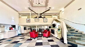 Een hotel lobby met een receptiebalie, zithoek, trap en een kroonluchter.