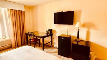 A hotel room with a bed, a desk, a chair, a television, a lamp, and a heater.