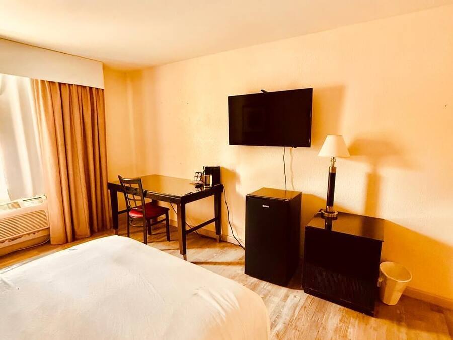 A hotel room with a bed, a desk, a chair, a television, a lamp, and a heater.