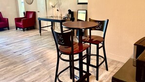 Een eetgedeelte met een ronde tafel en vier stoelen, een aan de muur bevestigde televisie, en een lijst met een afbeelding erboven.