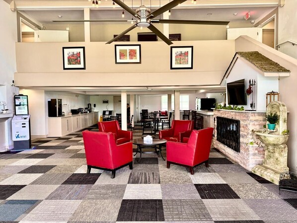 A hotel lobby with a check-in counter, red seating, a fireplace, and framed artwork on the walls.