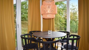 Une table ronde entourée de six chaises, un luminaire suspendu en fibres tressées et un vase en verre posé sur la table.
