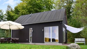 Une maison moderne à l’extérieur sombre, dotée de grandes portes-fenêtres coulissantes et d’un espace de détente extérieur couvert, avec une table et des chaises.