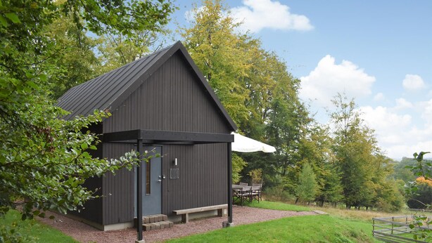 Un petit bâtiment en bois sombre, doté d’un toit en pente, d’une porte et d’un banc à l’extérieur.