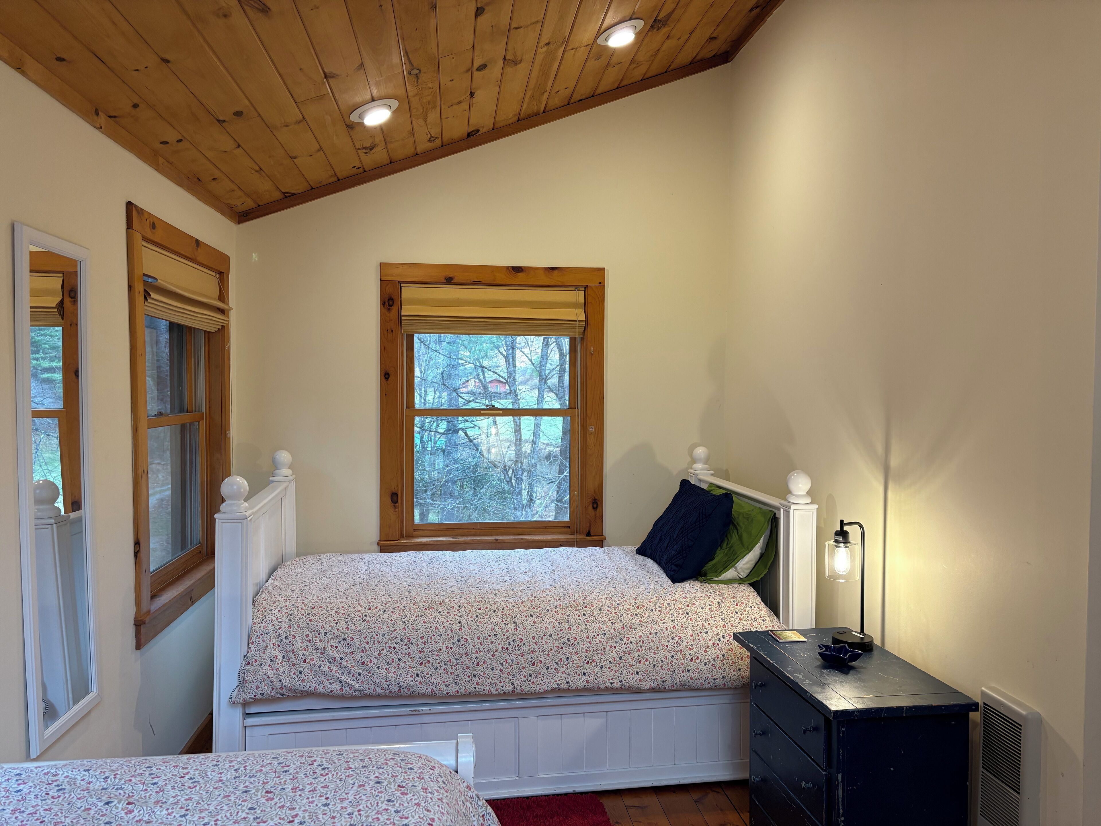 A bedroom with a bed, a nightstand, a window, and a wooden ceiling.
