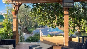 Un espacio al aire libre techado con mobiliario de mimbre, una piscina y un pérgola con plantas trepadoras.