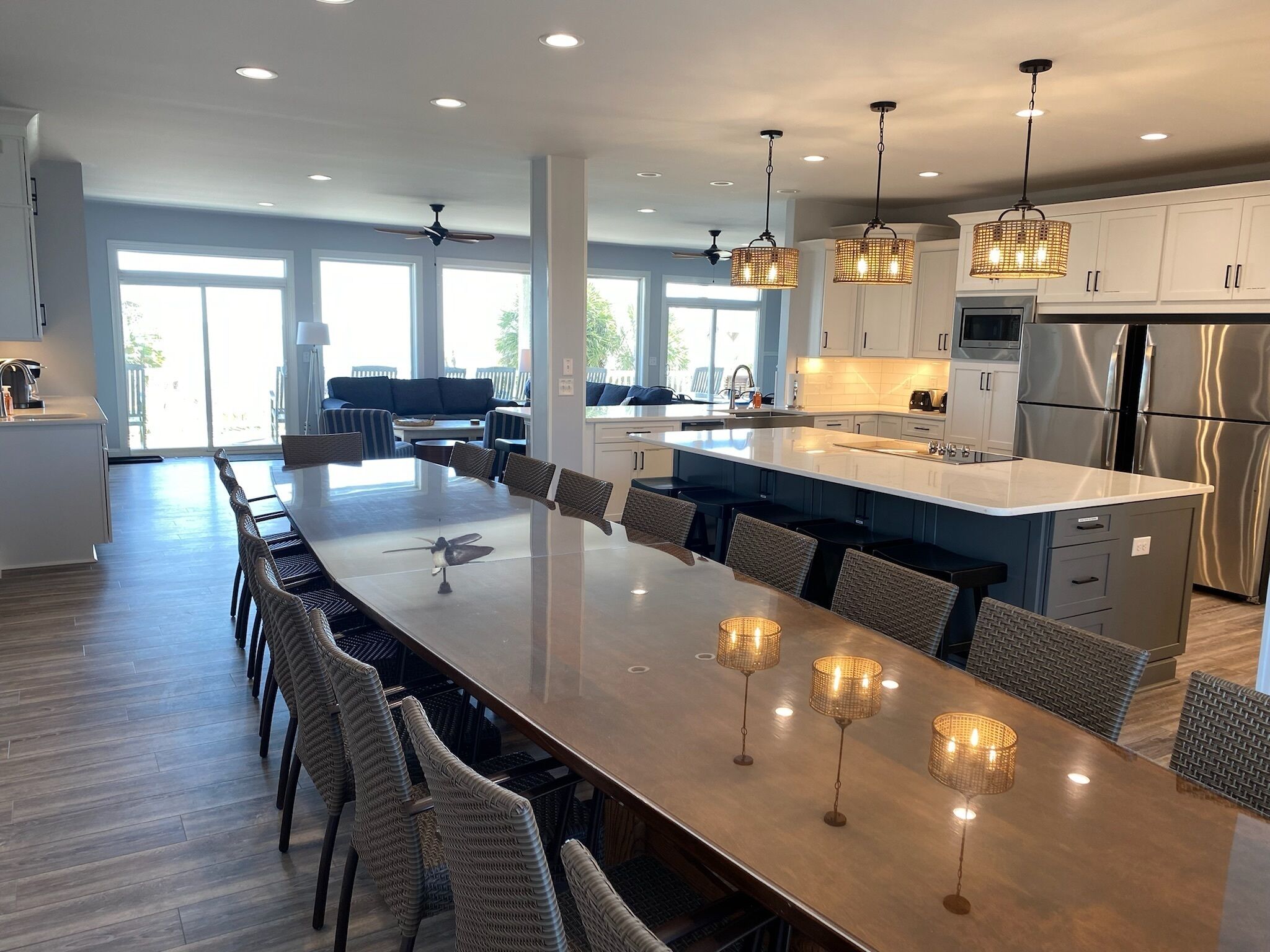 Una cocina amplia con una isla grande, electrodomésticos modernos y una zona de comedor con sillas de mimbre y luces colgantes.
