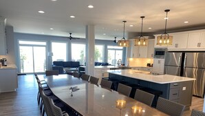 Une cuisine spacieuse dotée d’un grand îlot central, d’appareils électroménagers modernes et d’un coin repas avec des chaises en osier et des luminaires suspendus.