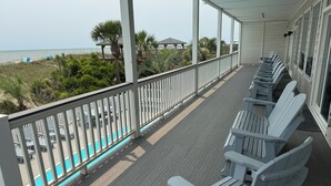 Une terrasse couverte avec des fauteuils Adirondack blancs, une piscine et une vue sur la plage et l’océan.