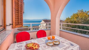 Un balcon avec une table préparée pour le petit-déjeuner, offrant une vue panoramique sur la mer et les collines.