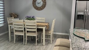 Une cuisine moderne avec un coin repas, comprenant une table en bois, des chaises, une horloge et un réfrigérateur en acier inoxydable.