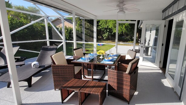 Une terrasse couverte, meublée de meubles en osier, avec une table dressée pour le repas, et une vue sur le jardin.