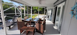 A covered patio with wicker furniture, a table set for dining, and a view of the backyard. - “Family Tides” Furnished Beach House w/HEATED Pool (Vero Beach)