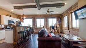 A spacious living area with a large leather sofa, a wooden coffee table, and a bar with stools. There is a kitchen area with modern appliances and a large window providing natural light. - In the Heart of Downtown Historic Hot Springs (Hot Springs)