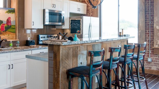 A kitchen with white cabinets, a central island with bar stools, a hanging light fixture, and a view through a window. - In the Heart of Downtown Historic Hot Springs (Hot Springs)