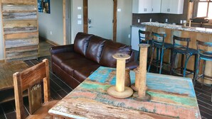 A rustic interior with a brown leather sofa, a wooden table with a colorful tablecloth, and a kitchen area with white cabinets and a bar stool. - In the Heart of Downtown Historic Hot Springs (Hot Springs)
