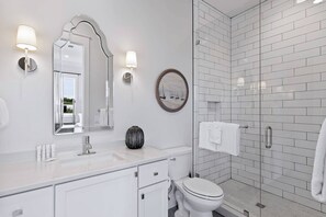 Une salle de bain moderne avec un meuble-lavabo blanc, un grand miroir, un miroir rond, des toilettes et une douche séparée par une paroi de verre.