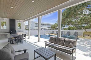 Une terrasse extérieure avec une piscine, un espace barbecue et un coin salon comprenant un canapé et des tables.