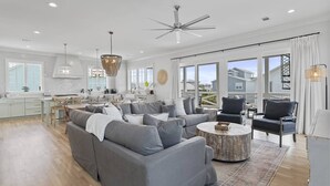 A spacious living room with a grey sofa, a round coffee table, and a dining area with a white table and chairs. - Grayton Home with Pool, Rooftop Deck & Fire Pit (Santa Rosa Beach)