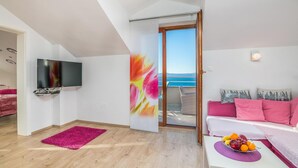 A modern room with a TV, a pink sofa, a dining table with fruit, and a balcony with a view of the sea. - Awesome apartment in Njivice with WiFi (Njivice)