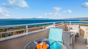 A balcony with a glass table, wicker furniture, and a view of the sea and distant mountains. - Awesome apartment in Njivice with WiFi (Njivice)