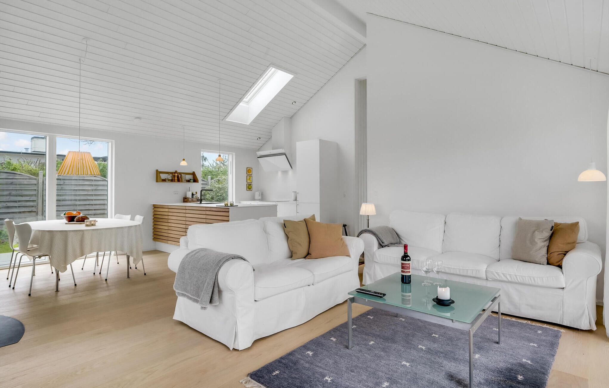A modern living room with a white sofa set, a glass coffee table, and a dining area with a white table and chairs.