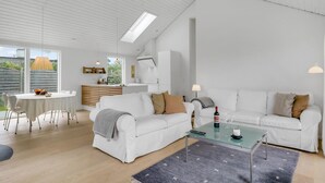 A modern living room with a white sofa set, a glass coffee table, and a dining area with a white table and chairs. - Stunning home in Vejby with kitchen (Vejby)