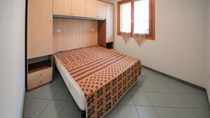 A bedroom with a bed, wooden wardrobe, and a window with curtains. - Stunning apartment in Rosolina Mare (Rosolina Mare)