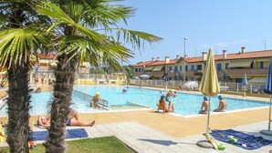 A swimming pool area with palm trees, tiled flooring, and umbrellas. - Stunning apartment in Rosolina Mare (Rosolina Mare)