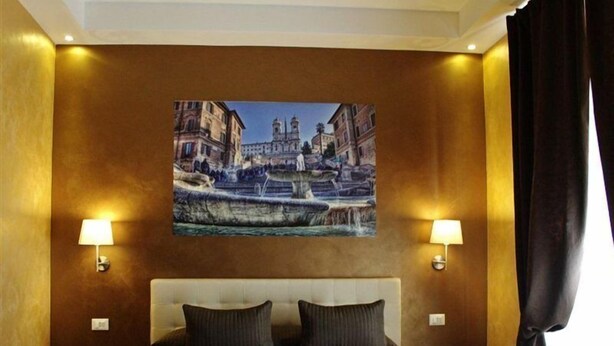 Quarto de hotel com uma cama grande, duas luminárias de cabeceira e um quadro de uma paisagem urbana na parede.