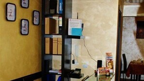 Uma receção com um computador, uma estante de livros e um relógio na parede.