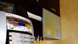 Máquina de café com várias opções de bebidas, uma chávena de café e um recipiente com cereais.