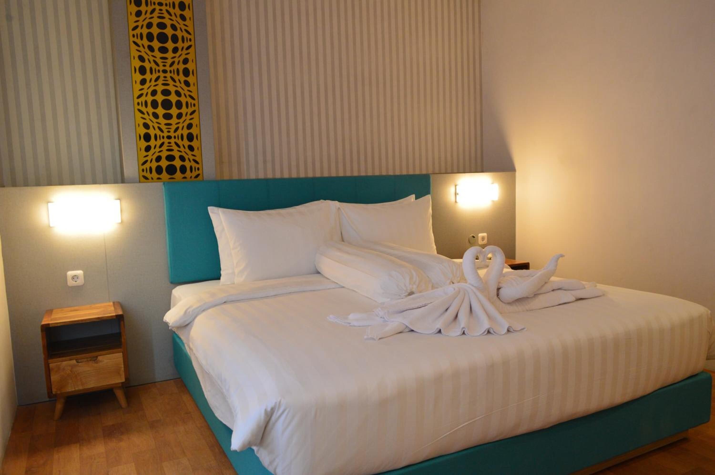 Habitación de hotel con cabecera color turquesa, ropa de cama blanca y un par de cisnes hechos con toallas sobre la cama.