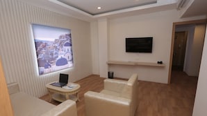 Ein modernes Wohnzimmer mit einem Flachbildfernseher, einem Laptop und einem großen Fenster mit Blick auf eine Küstenstadt.