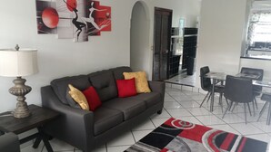 A modern living room with a grey sofa, red and gold cushions, a patterned rug, and abstract wall art. - Spacious Apartment with Essential Utensils for Cooking and Relaxation (nassau)