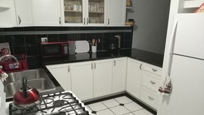 A kitchen with white cabinets, a gas stove, a microwave, and a refrigerator. - Spacious Apartment with Essential Utensils for Cooking and Relaxation (nassau)