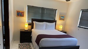 A bedroom with a bed, two bedside tables, a patterned rug, and two wall-mounted lamps. - Spacious Apartment with Essential Utensils for Cooking and Relaxation (nassau)