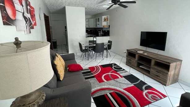 A modern living room with a grey sofa, a red and black rug, a wooden TV stand, and a ceiling fan. - Spacious Apartment with Essential Utensils for Cooking and Relaxation (nassau)