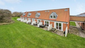 Une rangée de maisons de plain-pied, avec des toits couverts de tuiles rouges et des fenêtres à cadre blanc, chacune dotée d’un petit balcon.
