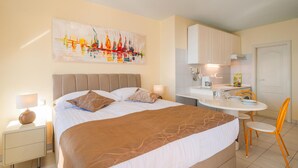 Ein Hotelzimmer mit einem großen Bett, einer kleinen Küchenzeile, einem Essbereich und einem Gemälde an der Wand.