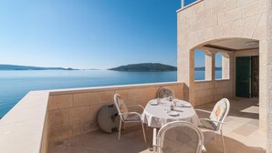 Eine Terrasse mit Tisch für zwei Personen, Blick auf ein ruhiges Meer und sanfte Hügel in der Ferne.