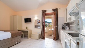 Habitación de hotel con cama, escritorio, silla, kitchenette y vistas al exterior.