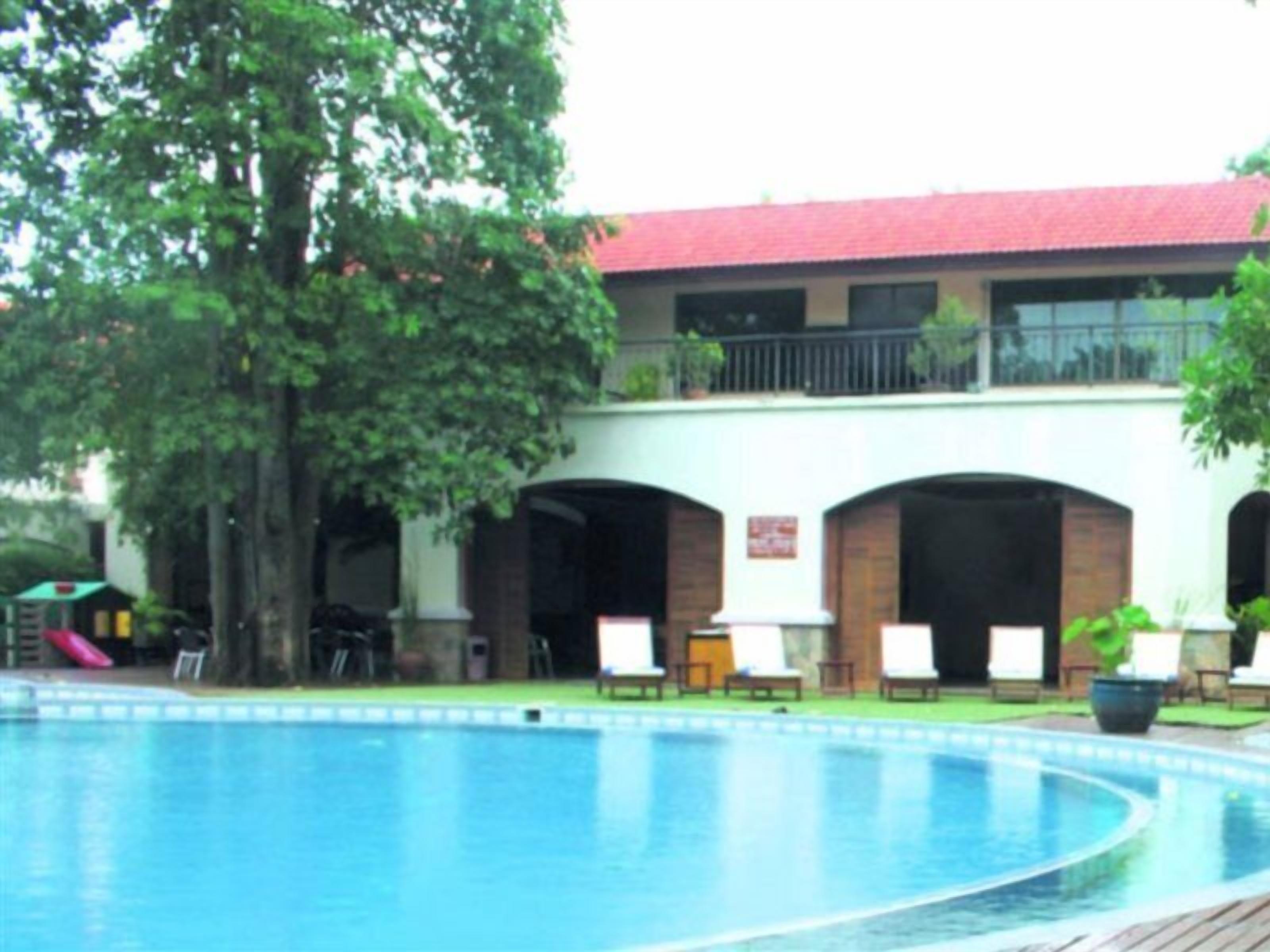 Un área de piscina con un edificio de techo rojo, asientos al aire libre y un árbol.
